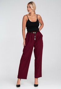 Bordowe spodnie z szerokimi nogawkami i plisami, zestawione z dopasowanym czarnym topem na ramiączkach. Posiada czarny pasek z złotą klamrą z logo oraz wysokie obcasy.