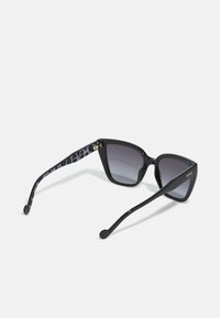 Black cat-eye sunglasses with gradient gray lenses. Glossy plastic frames, purple patterned arms. Gold brand logo on one side.
