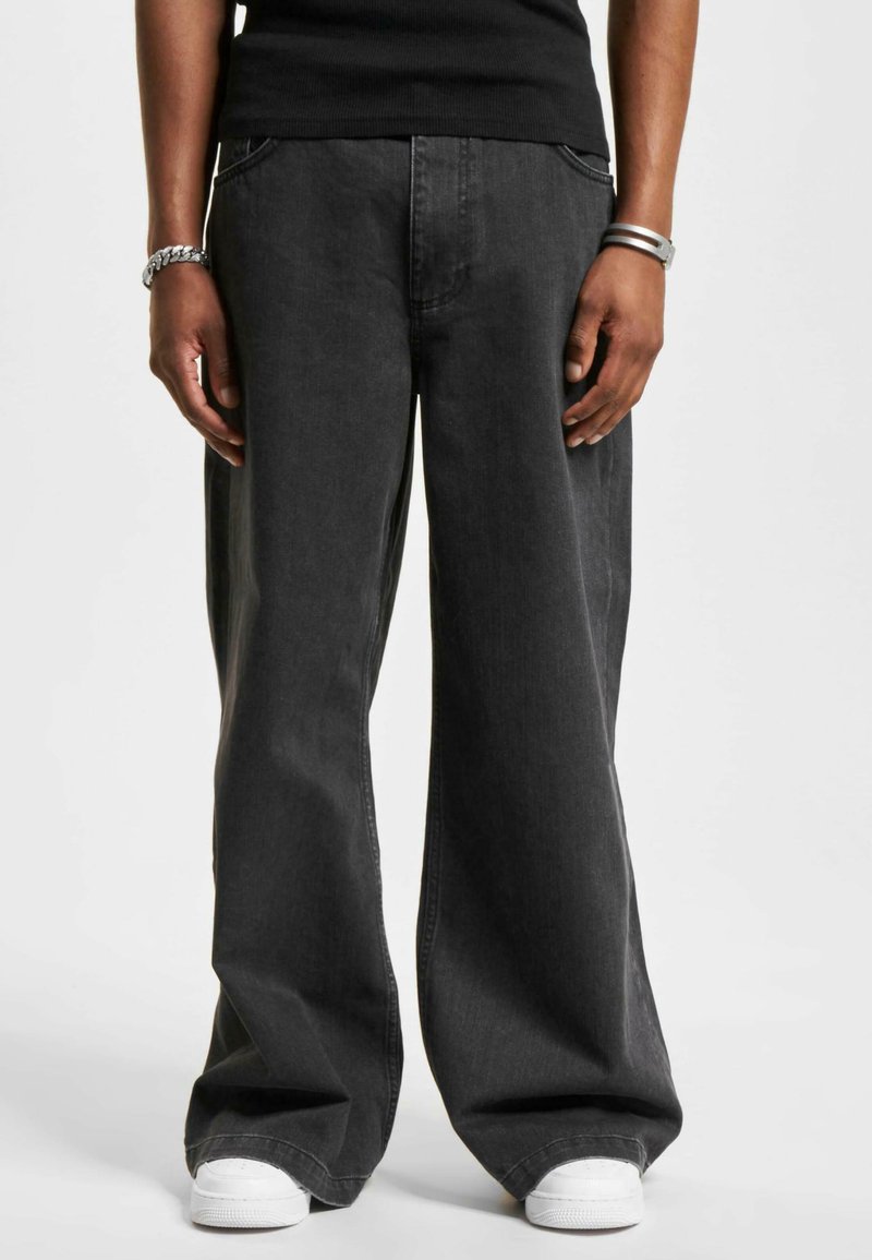 Pantalones de mezclilla de pierna ancha en gris oscuro con una textura suave, bolsillos delanteros y un ajuste relajado, combinados con zapatillas blancas.