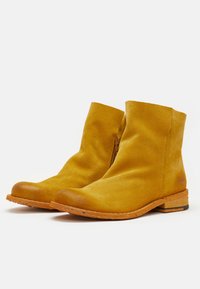 Botas de tobillo de ante amarillo con puntera de cuero marrón y cremallera lateral. La suela presenta una textura similar a la madera para mayor agarre y durabilidad.