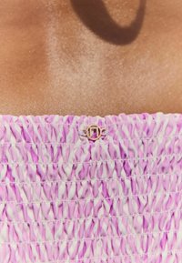 Tessuto arricciato viola e bianco, caratterizzato da una texture smock. Un piccolo dettaglio in metallo dorato è visibile nella parte superiore.