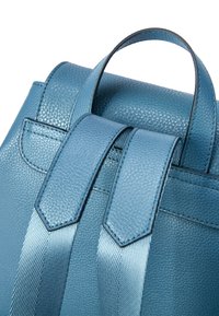 Zaino in pelle blu con finitura testurizzata, spallacci in satin a contrasto e manico superiore. La ferramenta presenta dettagli di cucitura sottili.