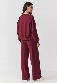 Burgundowy sweter i spodnie szerokie, wykonane z miękkiego materiału w luźnym kroju. Posiada okrągły dekolt i elastyczne wykończenia na mankietach.