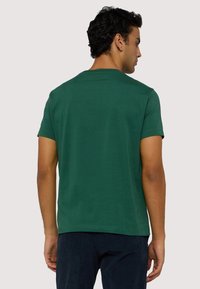 T-shirt verde a maniche corte realizzato in cotone, con classico collo rotondo e una texture liscia e uniforme, mostrato da dietro.