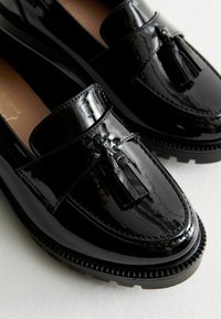 Svarta lackläder loafers med en dekorativ kvast, rund tå och tjock gummisula med texturerad detalj.