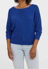 Pull en tricot bleu avec un large col bateau, manches longues dolman et ourlet côtelé. Associé à un jean délavé clair.