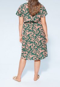 Vestido floral con un fondo verde y patrones botánicos en rosa, con mangas cortas y un corte relajado, mostrado desde la parte posterior.