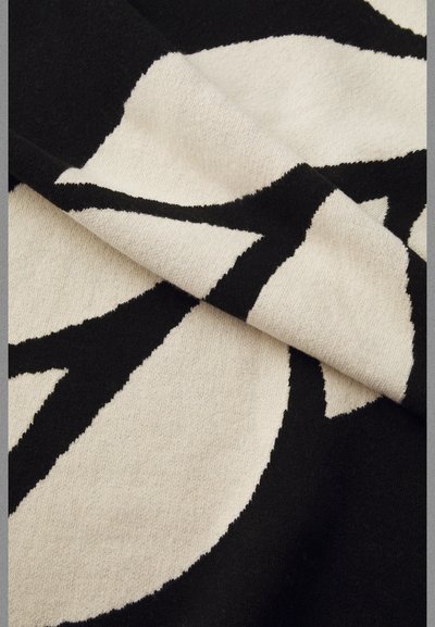 Fekete és krém színű textil, merész virágmintával, amely lágy, textúrált felületet és kontrasztos varrás részletekkel rendelkező éleket mutat.