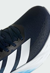 Close-up of a navy blue running shoe with white sole and three white stripes on the side, featuring dark blue laces and mesh upper.