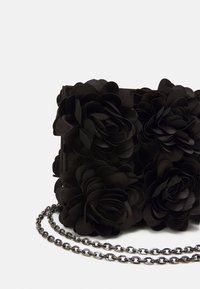 Pochette noire ornée d'appliqués floraux en relief, présentant une surface texturée, une bandoulière chaîne et une forme rectangulaire structurée.