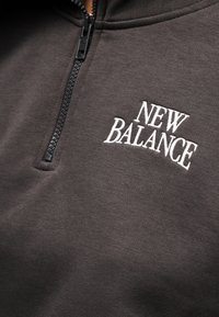 Sweat à capuche zippé gris foncé avec le logo "NEW BALANCE" brodé en blanc sur la poitrine gauche.