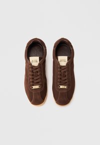 Pruun nahksneakerid ümarate varvastega, lipsudega disain, kuldse tooniga detailid ja kummi kummipõhi. Sile sisevooder.