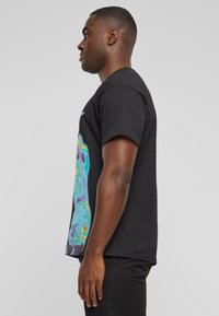 Czarny t-shirt z kolorową abstrakcyjną grafiką z boku. Krótkie rękawy, okrągły dekolt i luźny krój. Bawełniany materiał o gładkiej fakturze.