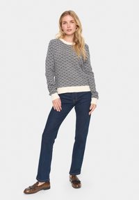 Kootud sviiter, millel on tume sinine ja valge ruudumuster, ribiga varrukad ja alumine äär; koos tumedate siniste teksade ja pruunide mokassiinidega.