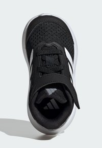 Scarpa sportiva nera con tomaia in mesh traspirante, dettagli testurizzati, cinturino regolabile e suola bianca con logo.