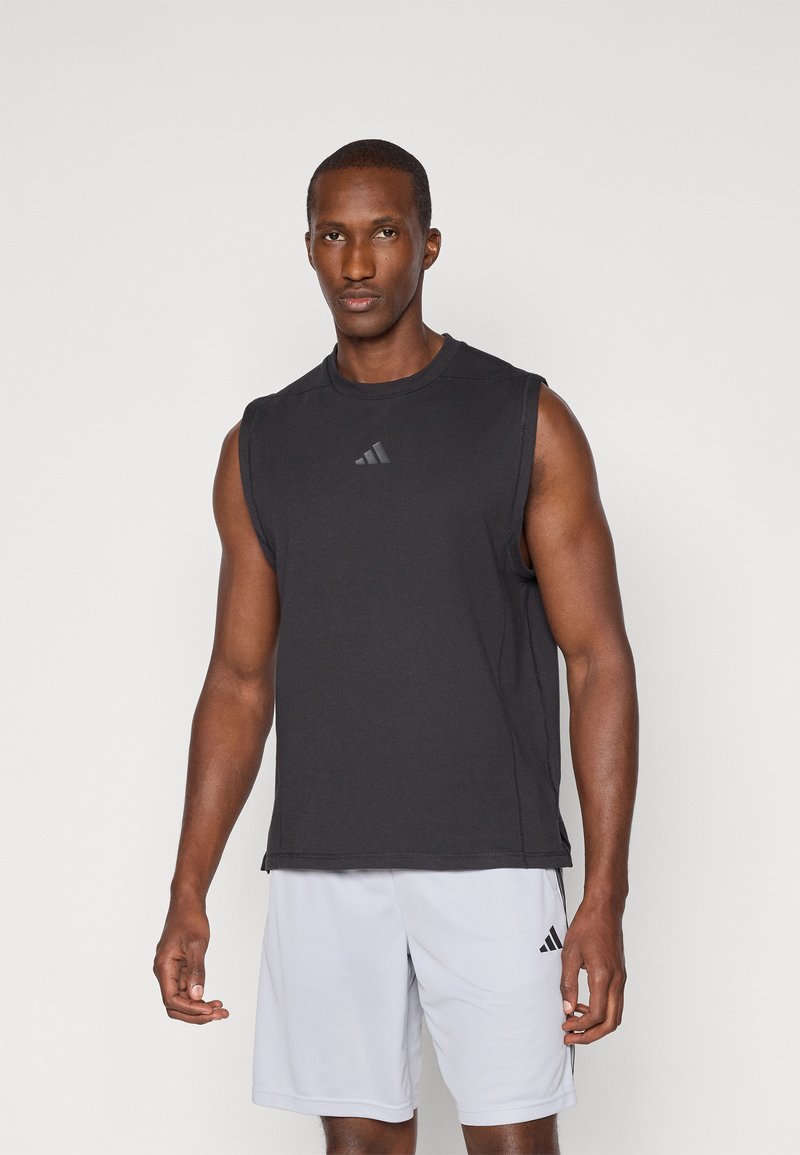 Top de sport sans manches noir avec un col rond et un logo subtil sur la poitrine. Porté avec un short gris clair arborant un petit logo.
