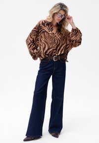 Bruine en crèmekleurige zebra-print blouse met opgestoken mouwen, gecombineerd met donkerblauwe flared jeans. Opvallende zilverkleurige riem en puntige schoenen.