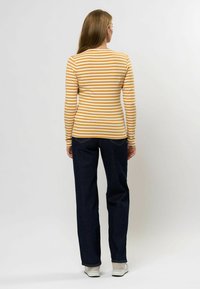 Cămașă cu mânecă lungă în dungi galbene și albe, cu un design ajustat, asortată cu blugi drepți negri și adidași deschiși la culoare.