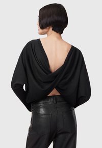 Black draped sweater with a deep V-back, long sleeves, and soft texture, paired with high-waisted black leather pants featuring back pockets.