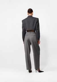 Sacou gri scurtat cu umeri căptușiți, asortat cu pantaloni gri în carouri, cu talie înaltă. Pantofii negri cu vârf ascuțit completează ținuta.