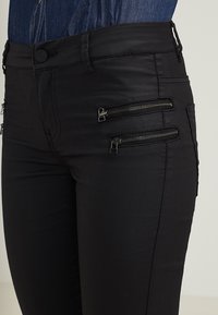 Černé skinny džíny s vysokým pasem, s dvěma zipovými kapsami na stehnech, vyrobené z hladké a elastické tkaniny.