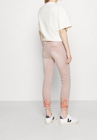 Jeans de color rosa claro con intrincados bordados naranjas en el dobladillo. Presenta un diseño de corte ajustado y un material de mezcla de algodón suave. Combinados con zapatillas blancas.