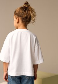 White oversized t-shirt made of cotton, short sleeves, crew neck, paired with blue denim jeans; simple and casual design.