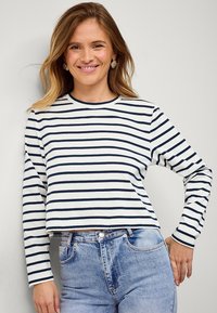 Gestreepte lange mouw shirt in wit en marineblauw, met een ronde halslijn, een ontspannen pasvorm en zacht materiaal. Gecombineerd met hooggeplaatste blauwe jeans.