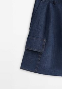 Jupe en denim bleu foncé avec une grande poche latérale rectangulaire avec des coutures visibles et un pli près de la ceinture.