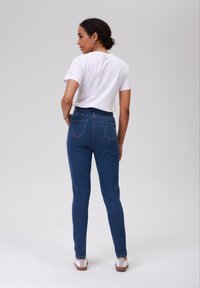 Jeans de ganga azul de cintura alta com um corte justo e bolsos traseiros, complementados por uma t-shirt branca de mangas curtas e sandálias.