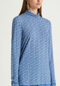 Haut bleu à manches longues avec un motif géométrique de carrés entrelacés, tissu doux, col montant et coupe ajustée.