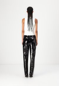 Pantalons en sequins noirs avec une surface brillante et texturée, associés à un haut sans manches blanc ajusté. Vue de dos.