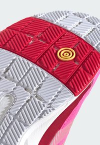 Semelle de chaussure avec un motif en caoutchouc rouge et blanc, présentant des grips texturés et un détail circulaire jaune au centre.