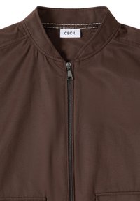 Veste marron avec col montant, fermeture éclair noire et étiquette de la marque "CECIL" à l'intérieur du col.