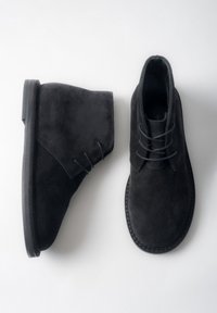 Czarne zamszowe botki za kostkę o gładkiej fakturze, zaokrąglonym nosku i sznurowanym zapięciu. Charakteryzują się płaską podeszwą i minimalną liczbą przeszyć.