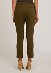 Spodnie w oliwkowym kolorze, dopasowane, o gładkiej fakturze i wąskim kroju, z dwiema tylnymi kieszeniami, w połączeniu z jasnobrązowymi sandałami na obcasie z odkrytymi palcami.