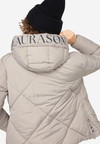 Lys beige pufferjakke med struktureret overflade, skrå quiltning, hætte og "LAURASON" broderet i mørkeblå på kraven.
