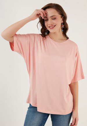 T-shirt oversize rosa chiaro con maniche corte, tessuto morbido, scollatura rotonda e vestibilità comoda. Abbinato a jeans blu.