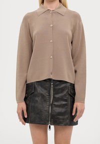 Brązowy sweter na guziki z dzianiny z kołnierzem, połączony z czarną skórzaną spódnicą z frontowym zamkiem błyskawicznym i dwiema bocznymi kieszeniami.