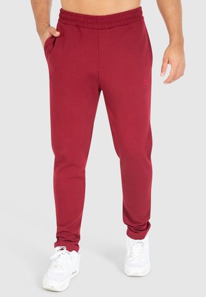 Bordeaux joggerbukser lavet af blødt stof, med en elastisk talje, sidelommer og en tætsiddende pasform, parret med hvide sneakers.