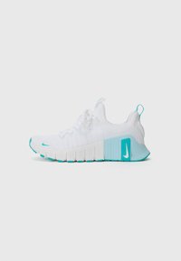 Hvit treningssko med teksturert overdel, turkise detaljer, en tykk s�åle, og en fremtredende Nike-logo på hælen. Snøring er til stede.