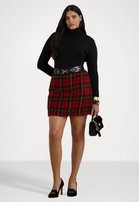 Melna kūkuma svītra, sarkana rūtainā mini svārki ar zaļiem akcents, melna ādas josta, melnas augstpapēžu kurpes ar zelta detaļām, turot nelielu somu.