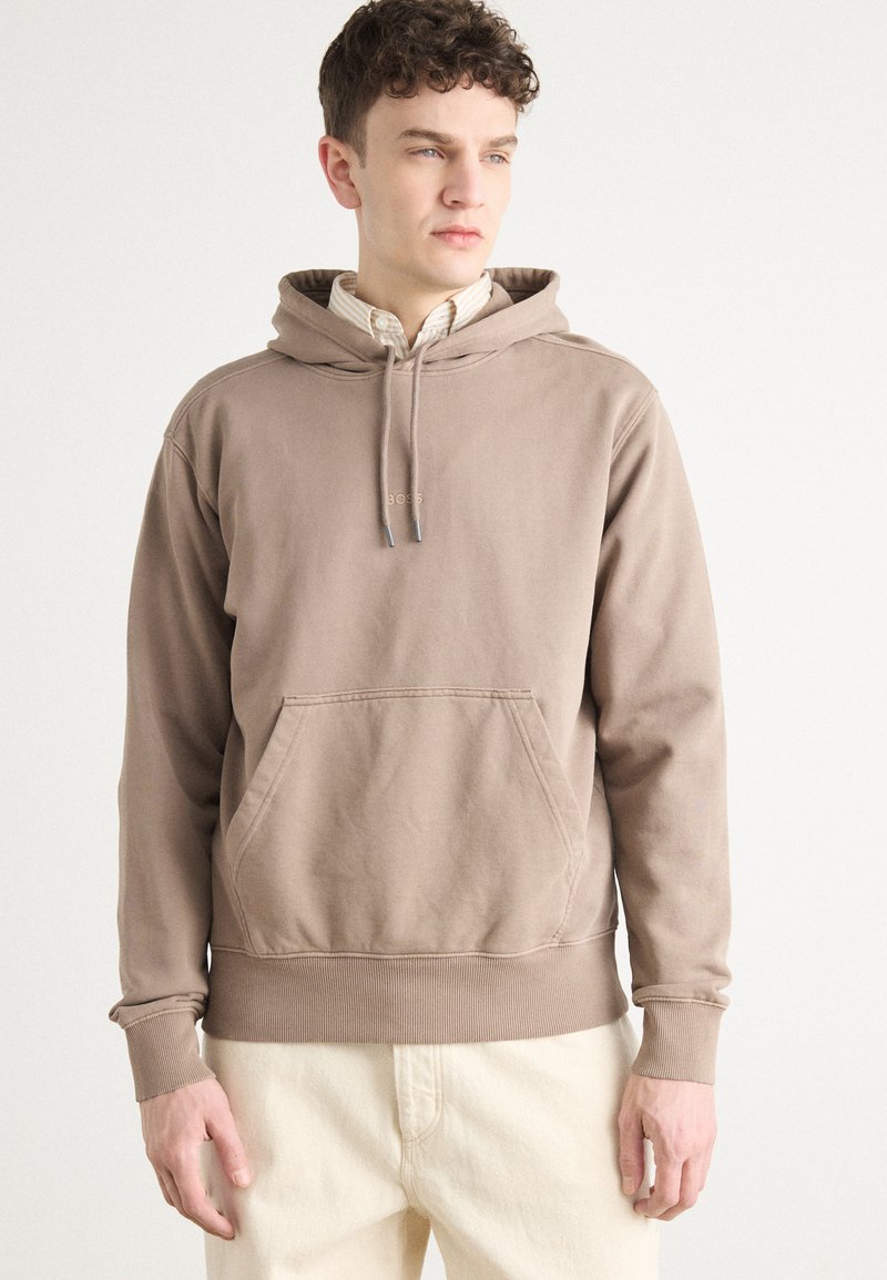 Bruine hoodie met een kangoeroezak, ribgebreide manchetten en zoom. Bevat een klein logo op de borst. Gedragen over een overhemd met kraag.