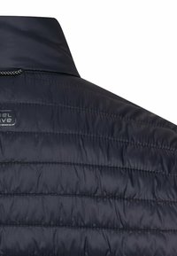 Dunkelblaue Steppjacke mit Schulter- und Kragenbereich, horizontal gesteppt und mit einem kleinen, teilweise sichtbaren Logo.