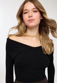 Top nero a coste con scollo a barca, maniche lunghe, caratterizzato da un design con colletto piegato e una silhouette aderente. Texture liscia.