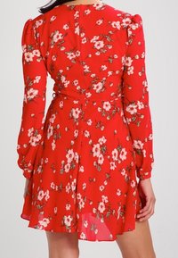 Vestido floral rojo con mangas abullonadas largas. Presenta patrones de flores en blanco y rosa, una cintura ajustada y una falda acampanada con una textura suave y transparente.
