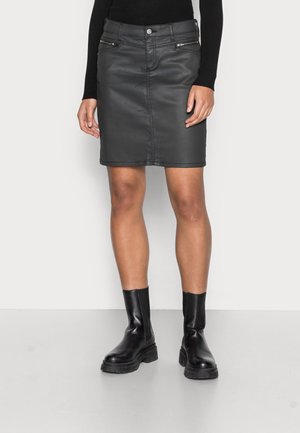 Jupe en cuir noir avec une coupe droite, dotée de deux poches avant zippées et d'une taille ajustée. Associée à des bottines noires.