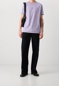 Fialové bavlněné tričko s krátkými rukávy a vyšitým logem "BOSS" na hrudi, spárované s tmavě modrými kalhotami širokého střihu a černými botami.