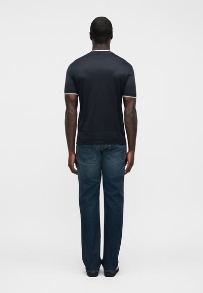 Σκούρο μπλε κοντομάνικο μπλουζάκι με λευκή λεπτομέρεια, συνδυασμένο με μπλε τζιν με ίσια μπατζάκια. Ορατές ραφές και κανονικές τσέπες στο τζιν.