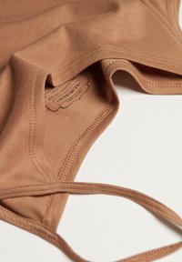 Camiseta sin mangas de algodón marrón con una textura suave, con escote redondeado y tirantes cruzados. Etiqueta visible en el interior.